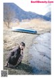 A woman sitting on the ground next to a body of water.