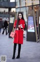 A woman in a red coat is standing on the street.