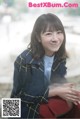 A young woman sitting on a stone wall smiling.