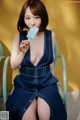 A woman in a denim dress eating a popsicle.