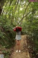 A woman in a gray dress and a red hoodie standing in the woods.