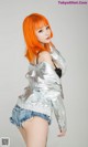 A woman with orange hair wearing a silver jacket and shorts.