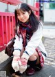 A young woman in a school uniform crouching down on the ground.