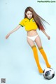 A woman in a yellow shirt and white panties kicking a soccer ball.