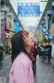 A woman in a pink jacket standing on a city street.