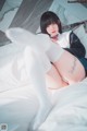 A woman in white stockings and a bow tie laying on a bed.