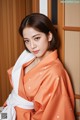 A woman in an orange and white kimono leaning against a wall.