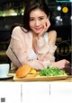 A woman sitting at a table with a hamburger and a cup of coffee.