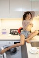 A woman sitting on top of a washing machine in a kitchen.