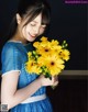 A woman in a blue dress holding a bunch of yellow flowers.