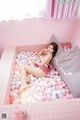 A woman laying in a bathtub filled with pink and white balloons.