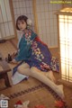 A woman in a kimono sitting on the floor next to a lamp.