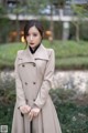 A woman in a beige trench coat holding an umbrella.